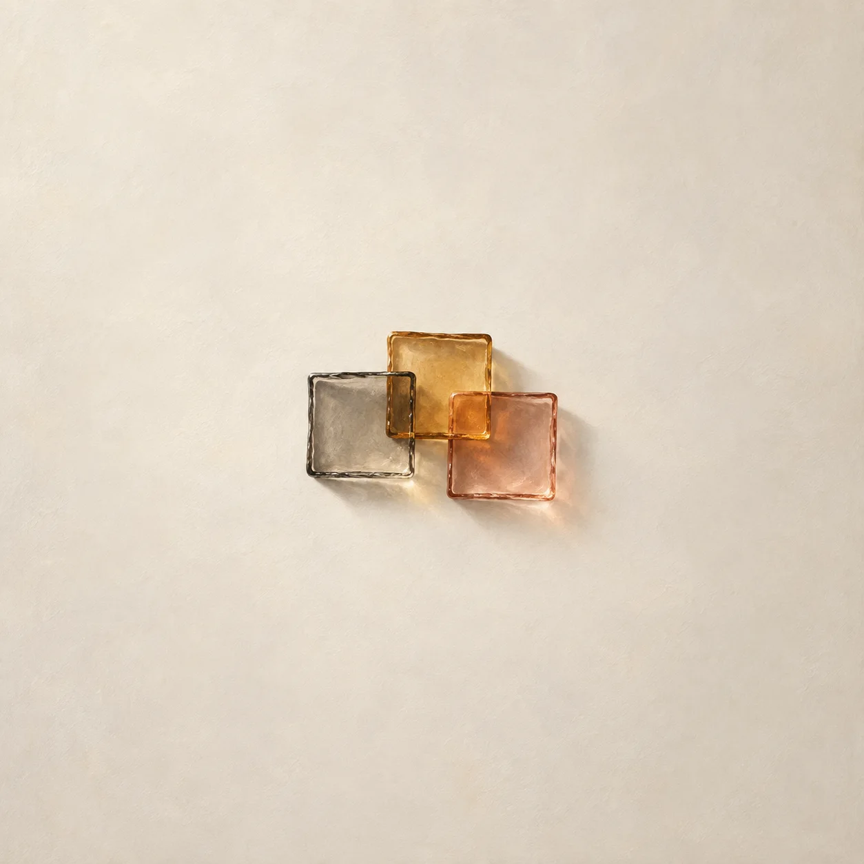 Three overlapping translucent glass squares in smoke grey, amber and rose, blurring the plain surface beneath them.