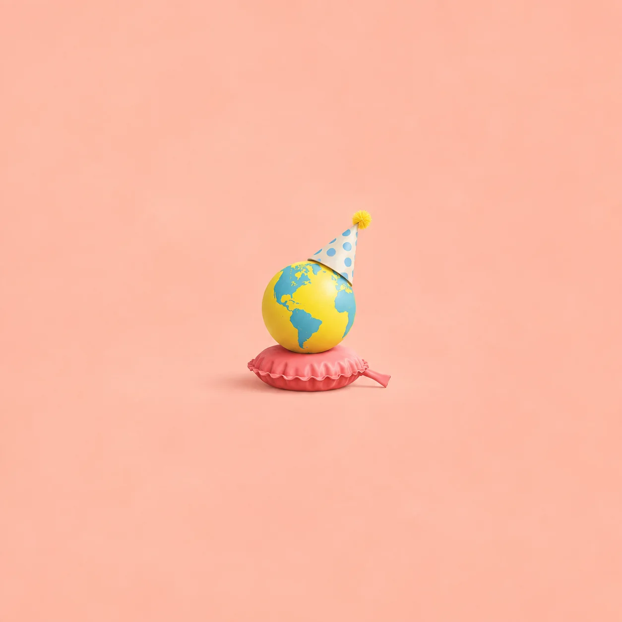 A yellow and blue globe wearing a spotted party hat rests on a pink whoopee cushion against coral.