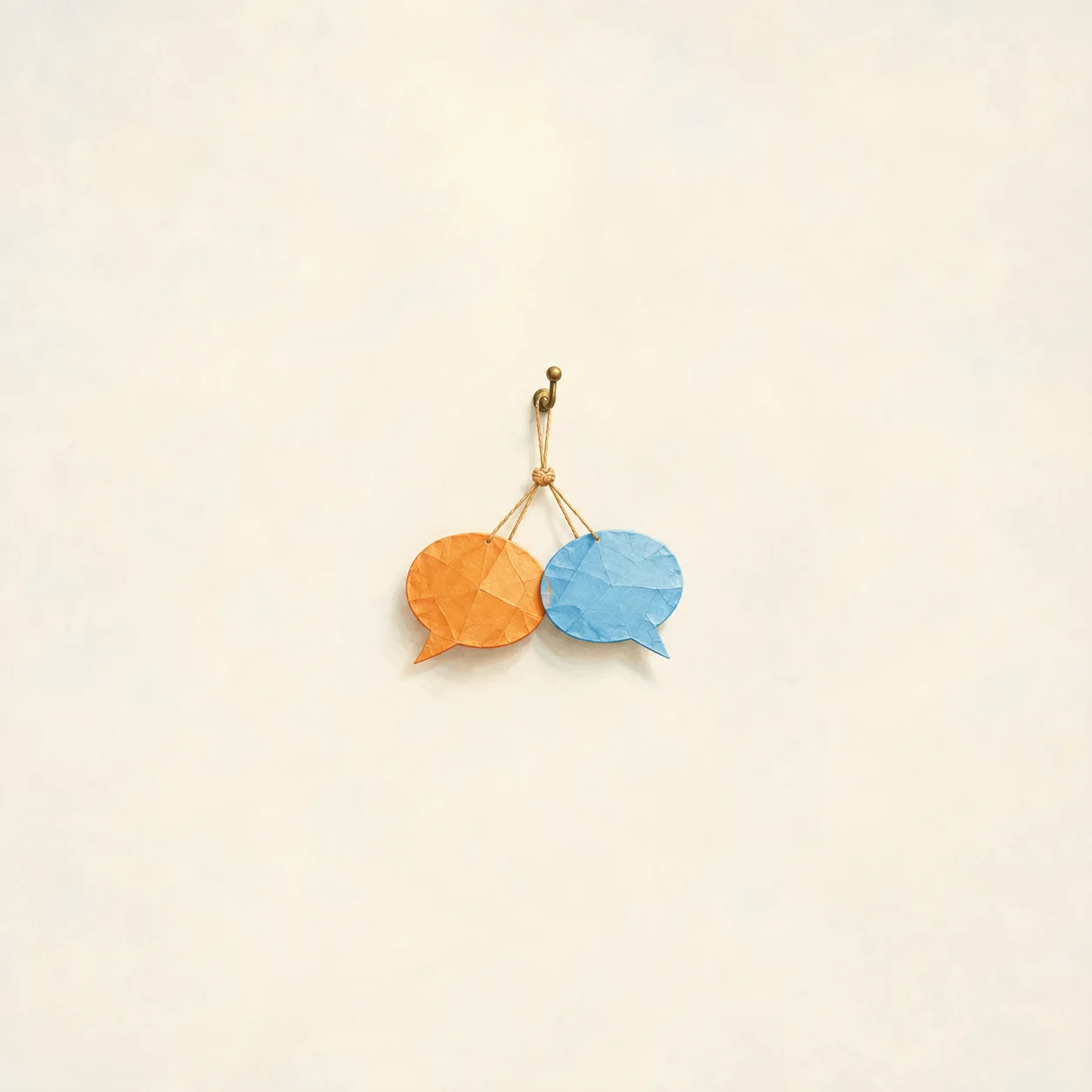 Orange and blue paper speech bubbles hang together by strings from a small hook against a cream background.