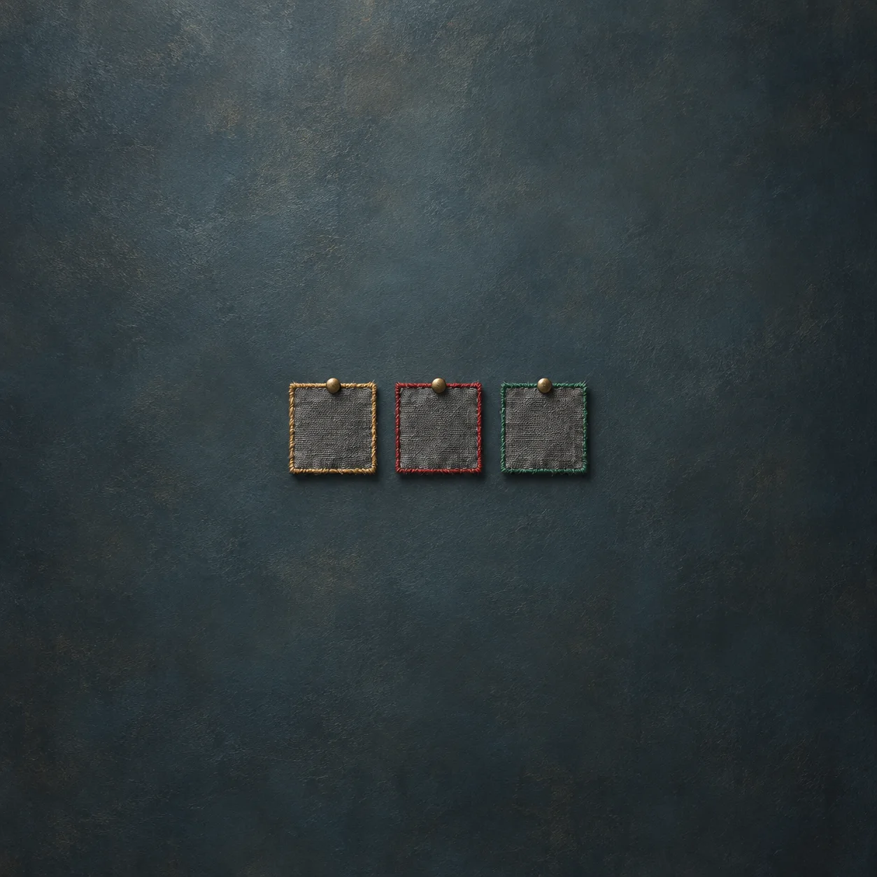 Three grey cloth patches pinned to a board, each edged with different colored thread: gold, red and green.