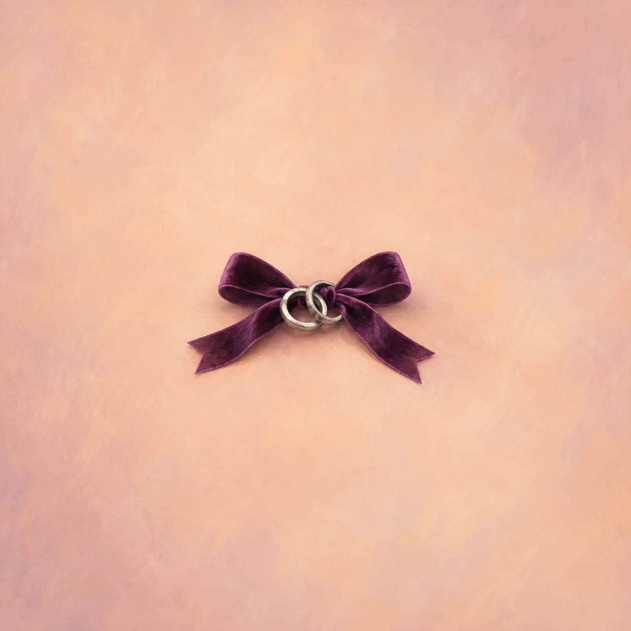 Two interlocked silver rings tied into a plum velvet bow against a soft peach background.