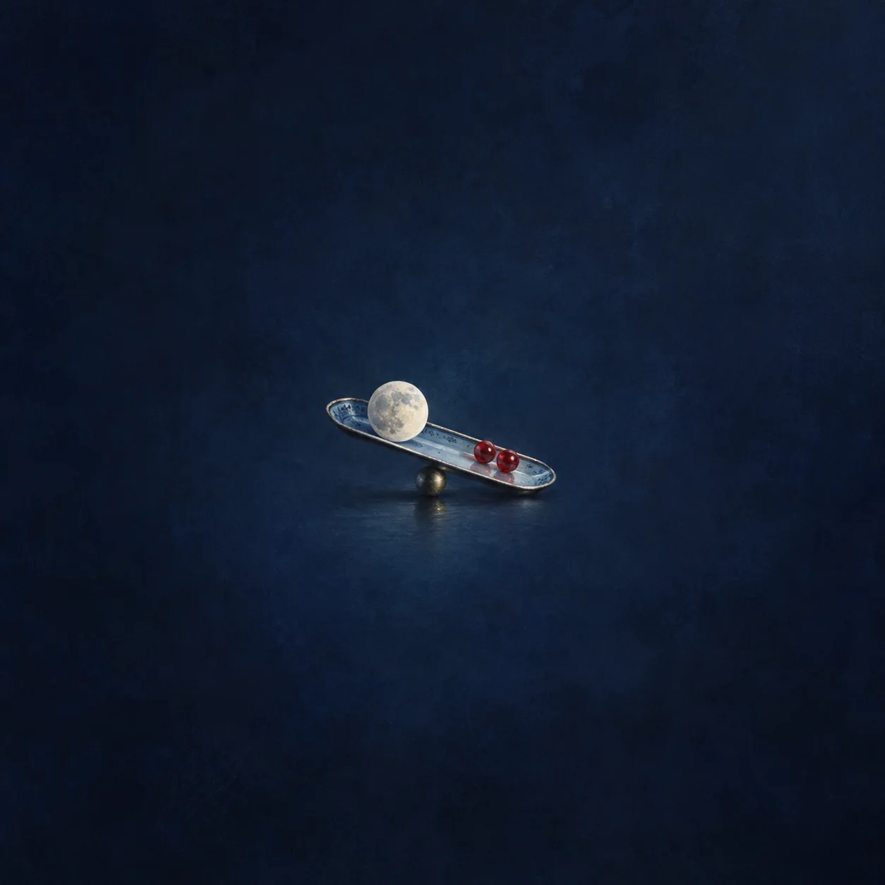 A tilted narrow tray balances a pale moon-like disc and two red glass beads against indigo.