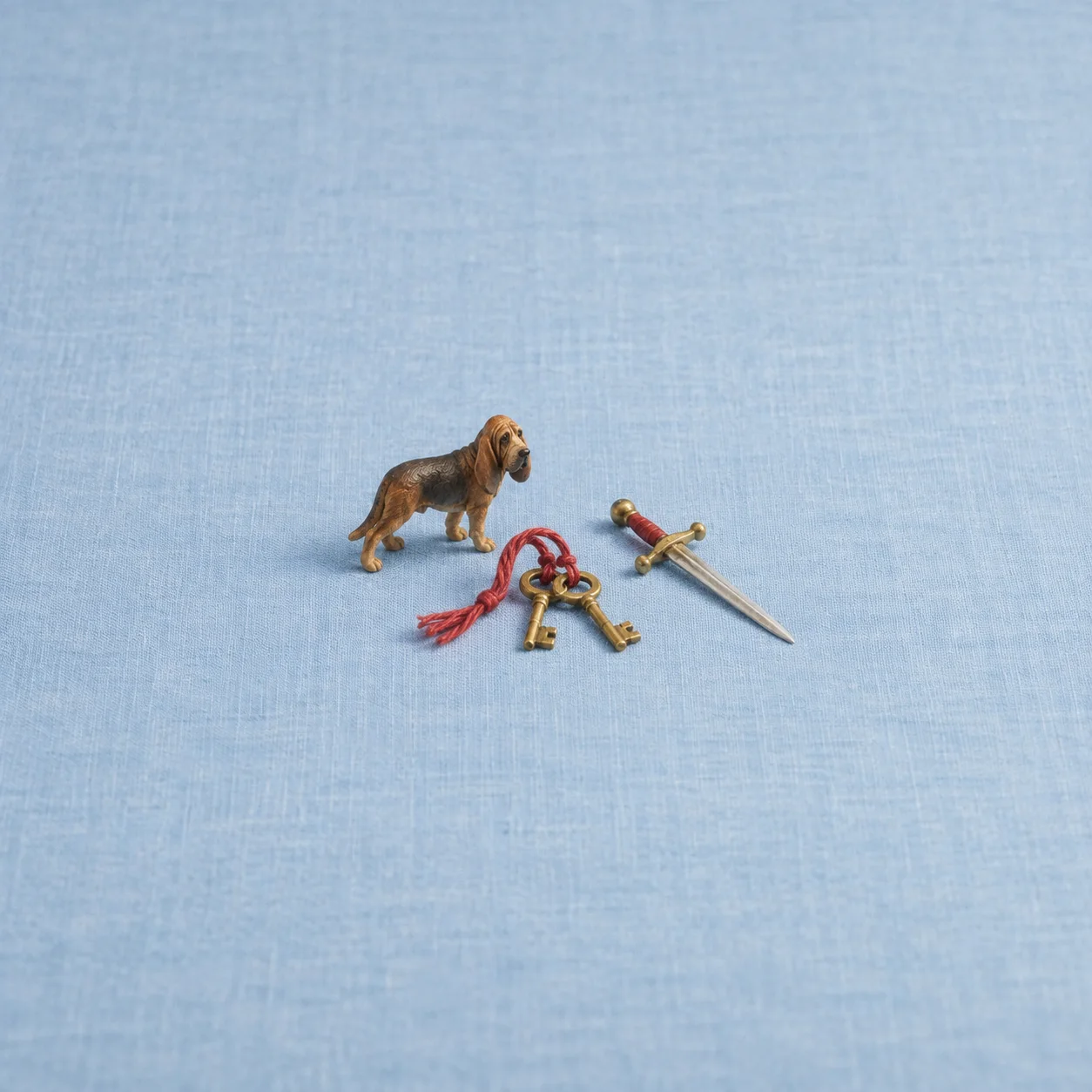 Two brass keys tied with red thread between a small toy hound and a toy sword on blue linen.