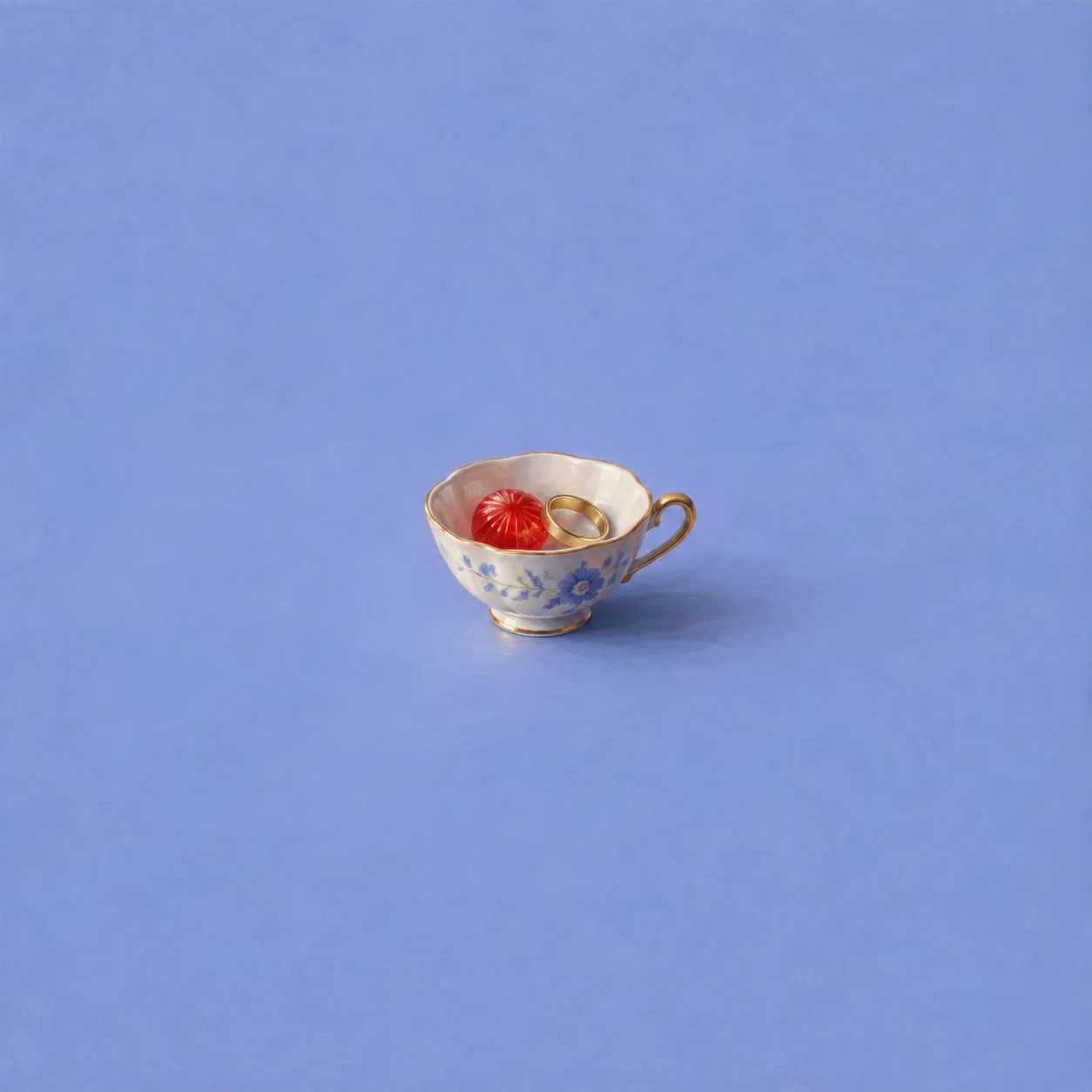 A patterned teacup holds a red sweet and a gold ring against periwinkle blue.