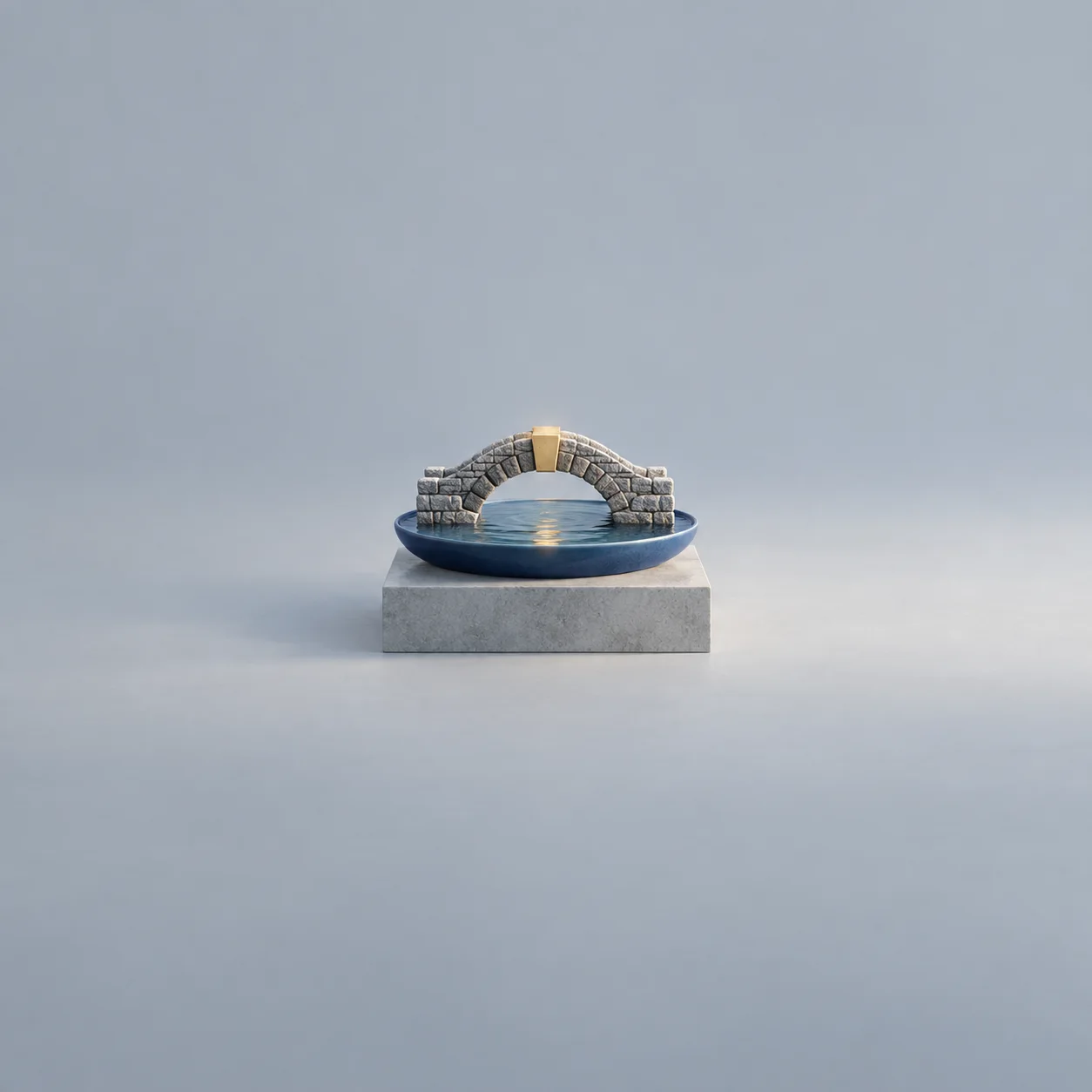 A miniature stone arch bridge with a gold-coloured keystone stands over a blue dish of water.