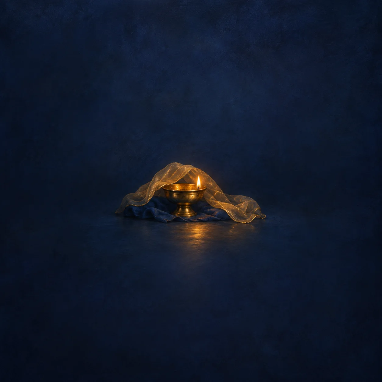 A small brass lamp burning beneath sheer golden fabric on indigo cloth.