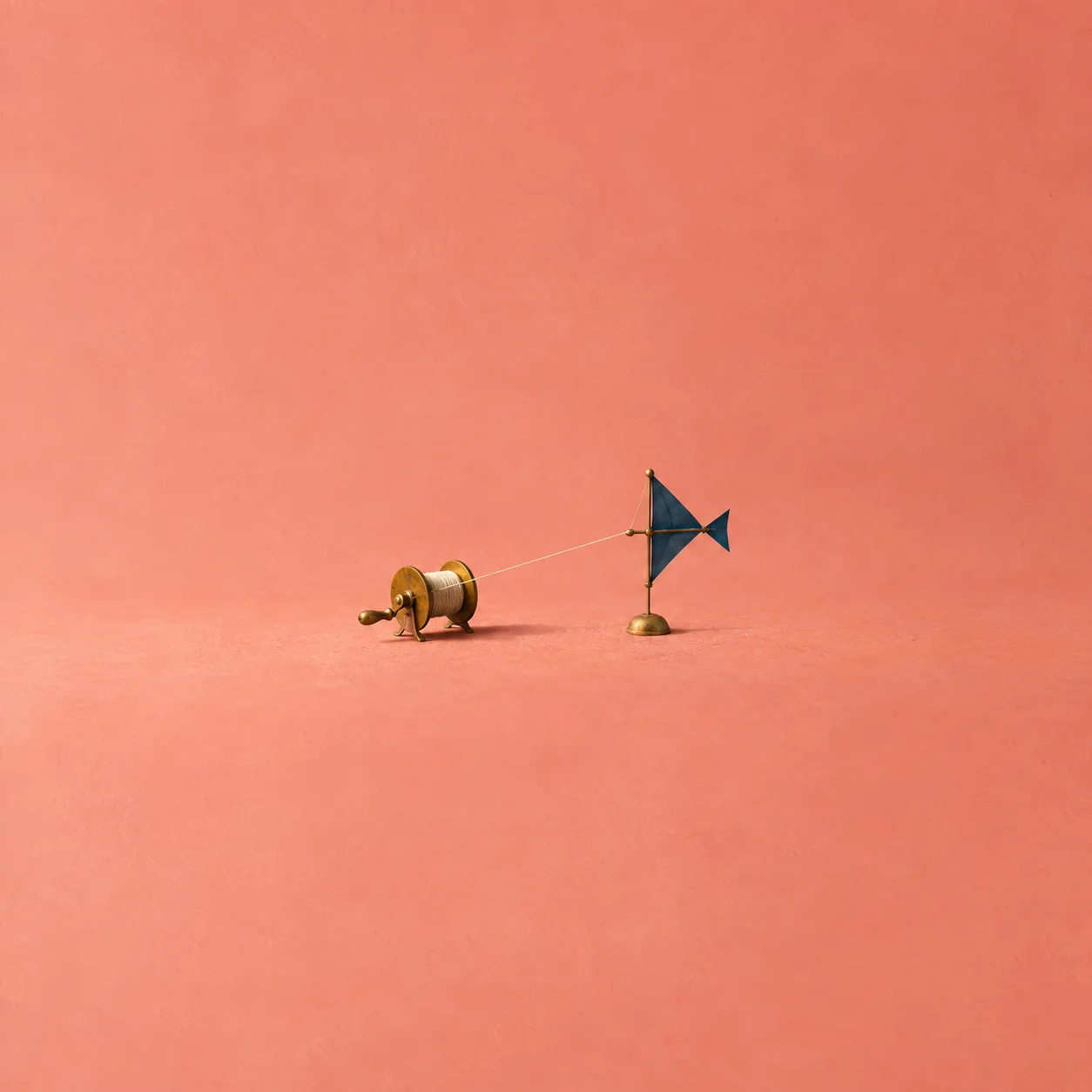 A small brass reel linked by taut thread to a miniature blue cloth sail on a coral surface.