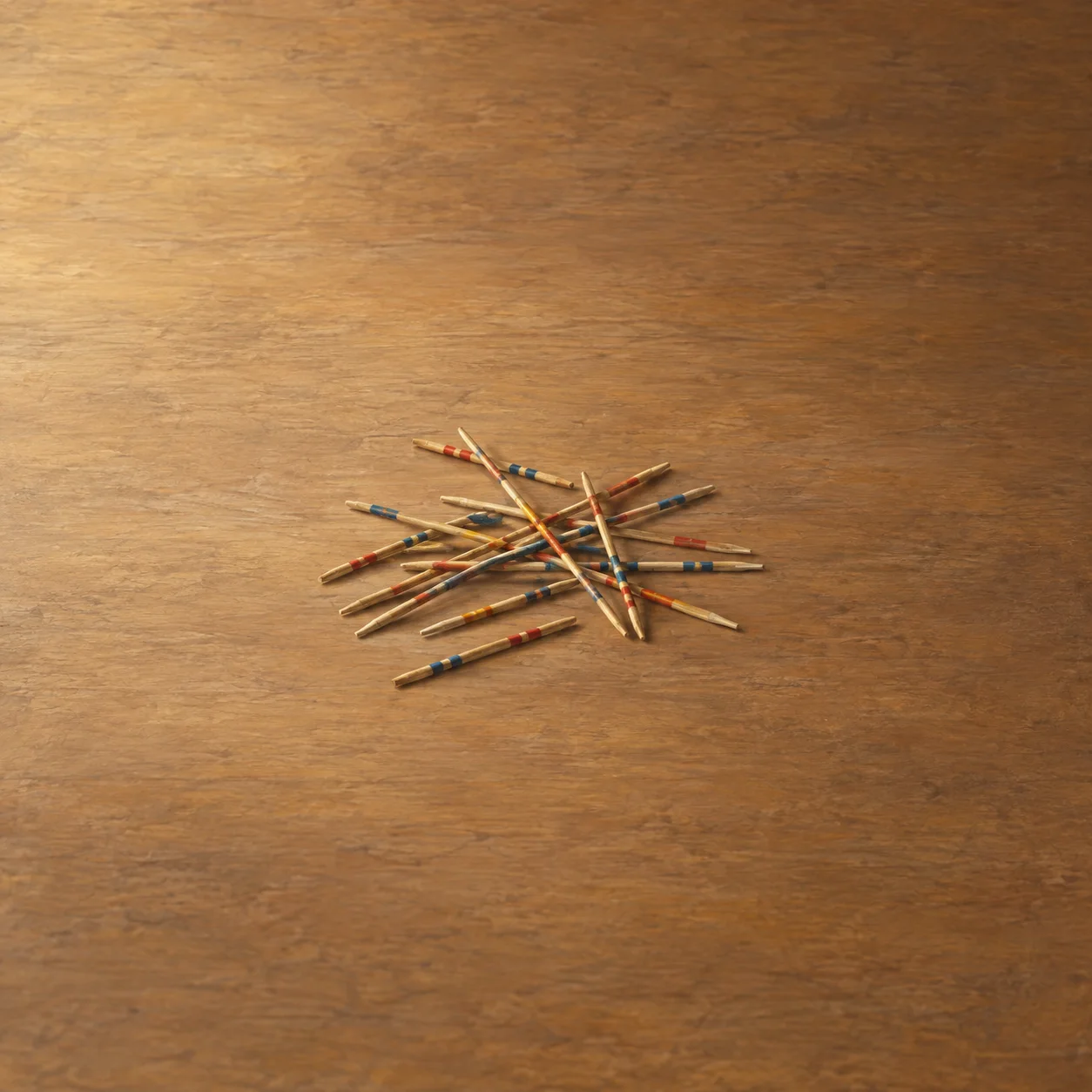 Wooden pick-up sticks with colored tips lie scattered across a warm wooden surface.