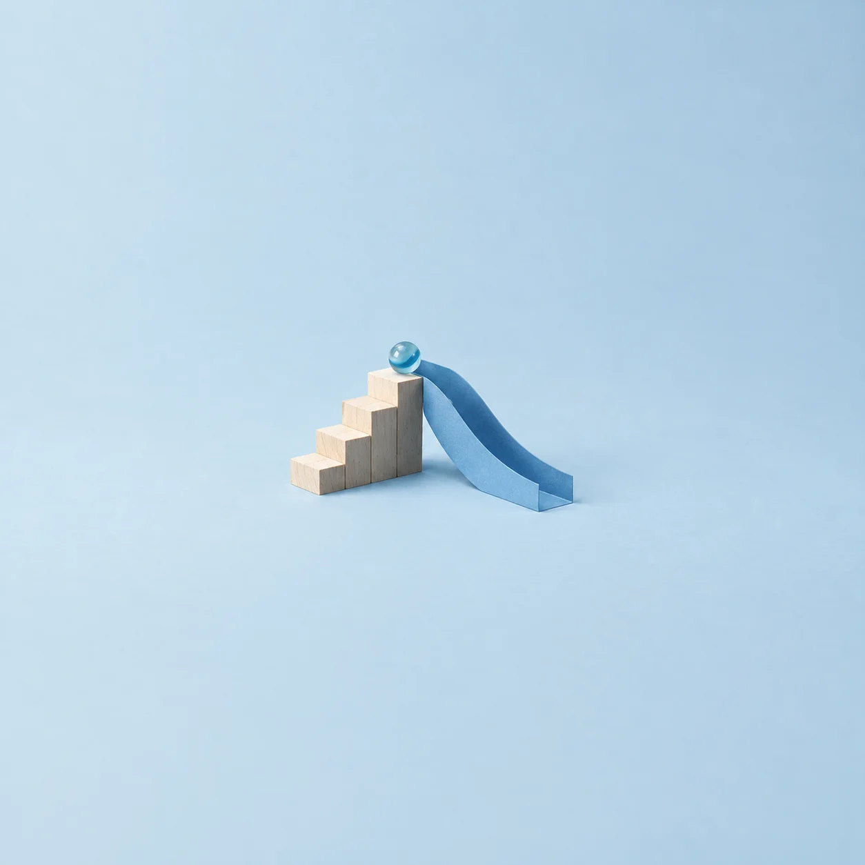 A small wooden block staircase with a marble at the top and a glossy blue chute sloping down.