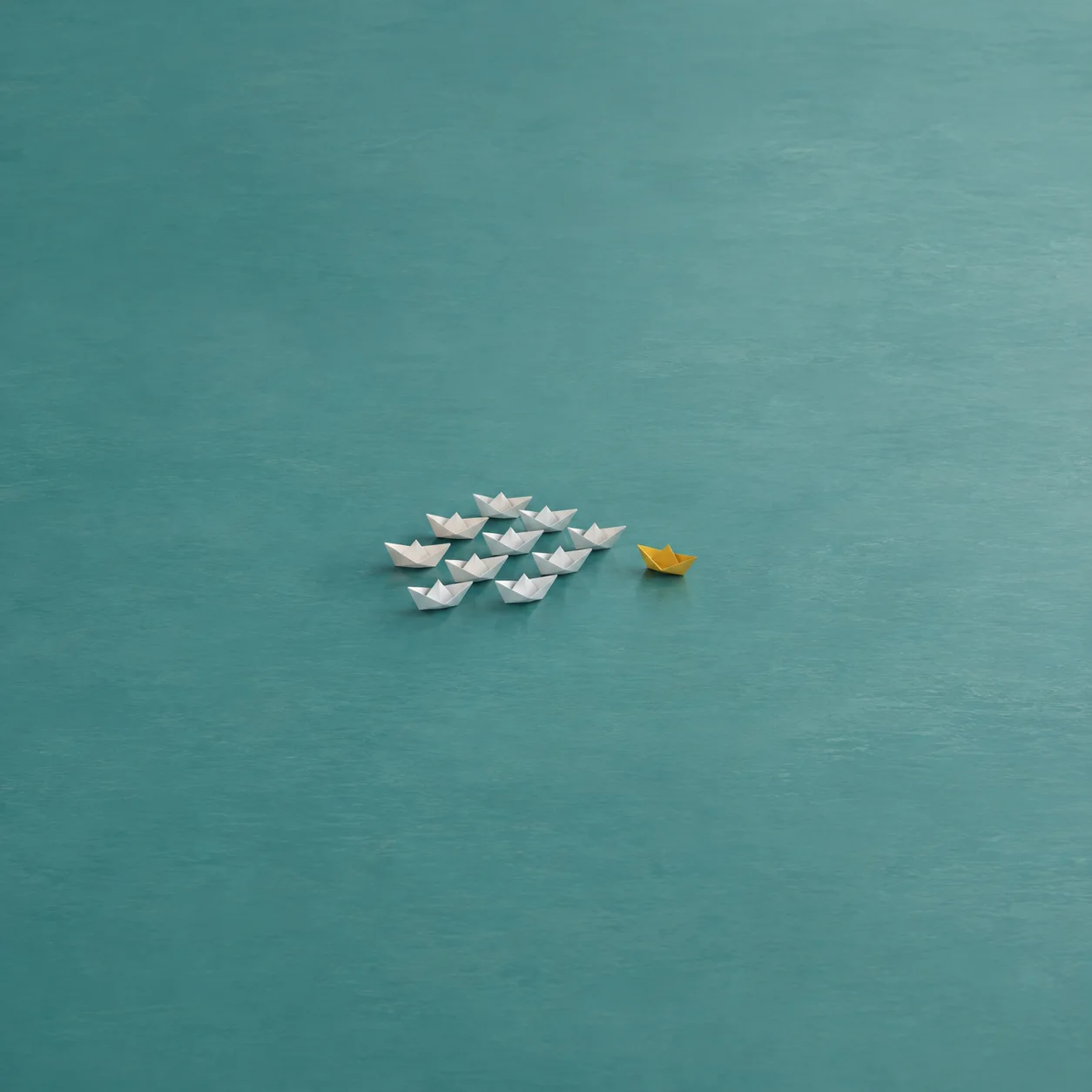 A group of white paper boats pointing right with one yellow paper boat turned sideways at the edge.
