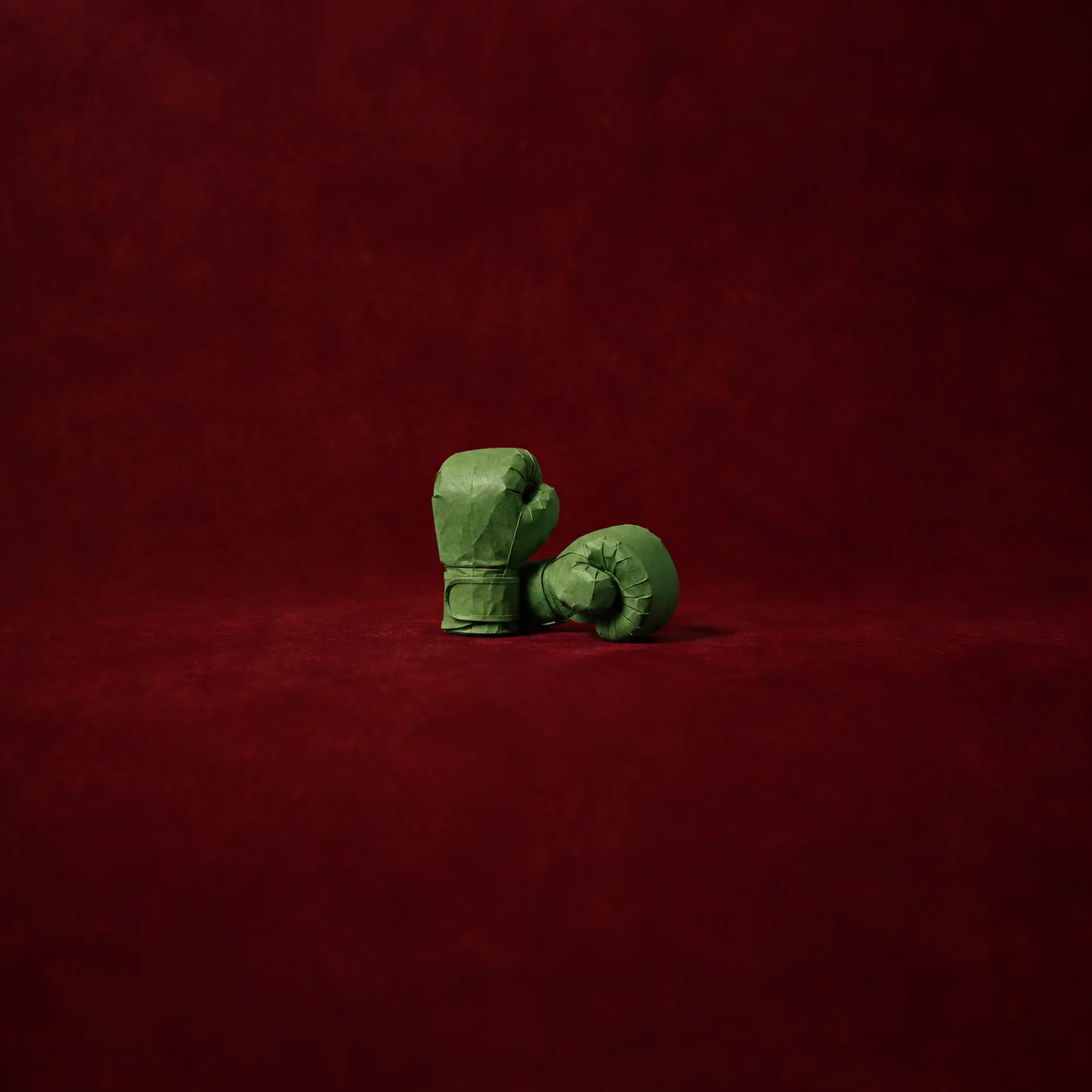 Sculptural green paper boxing gloves resting on oxblood velvet