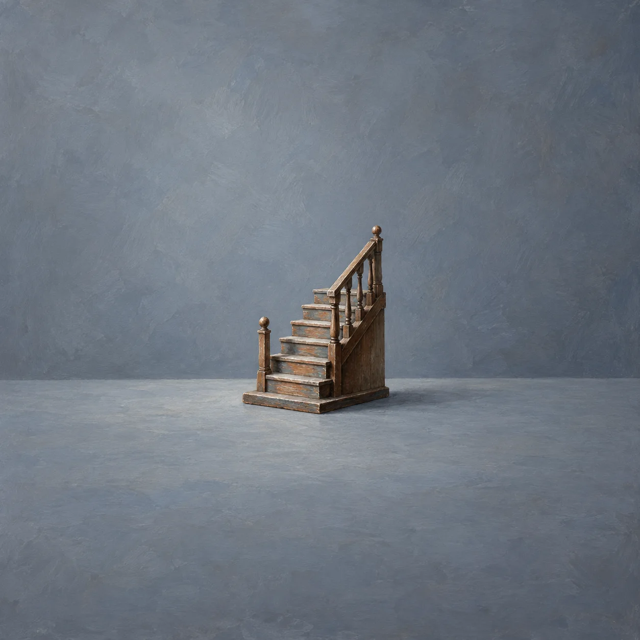 A miniature wooden staircase with a railing stands on a plain blue-grey tabletop.