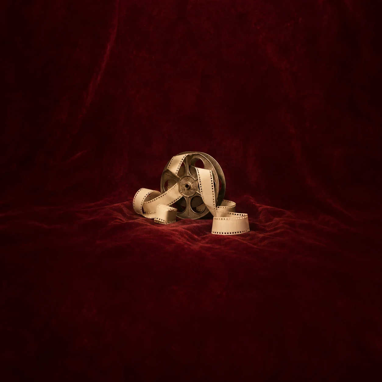 Painterly old film reel with a pale curling strip resting on burgundy velvet.
