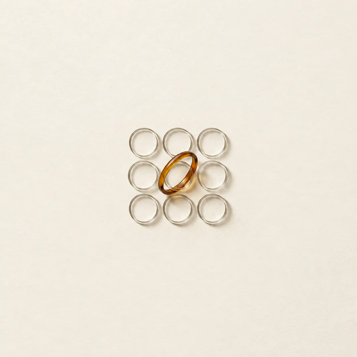 A single amber glass ring overlapping a small neat grid of empty rings on cream paper.