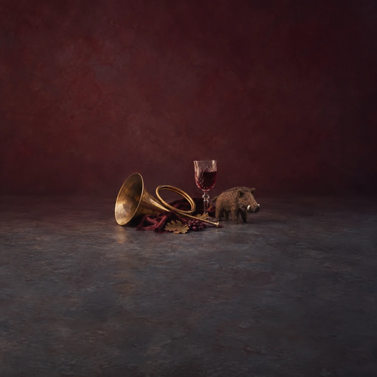 A brass hunting horn rests beside a wine glass, a small boar figure and dark red cloth.