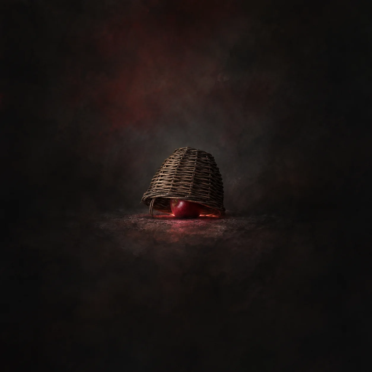A woven basket tipped over a red apple, with red light glowing at the gap, on a charcoal background.