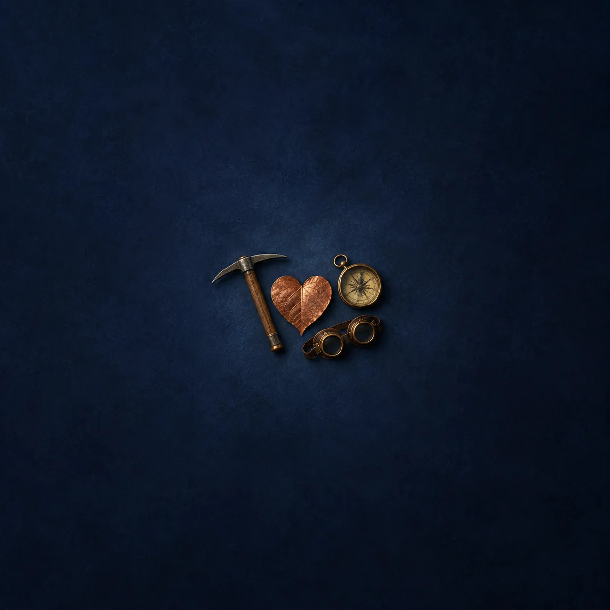 A small pickaxe, compass and goggles arranged around a copper heart-shaped leaf on indigo fabric.