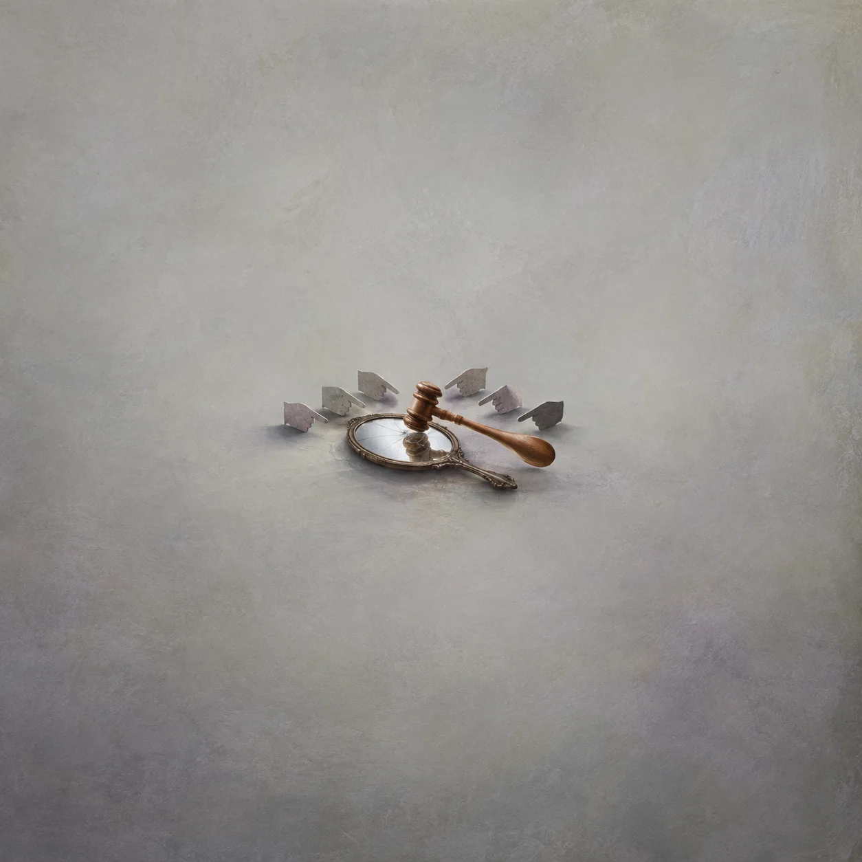 A wooden gavel lies on a hand mirror surrounded by grey paper shapes.