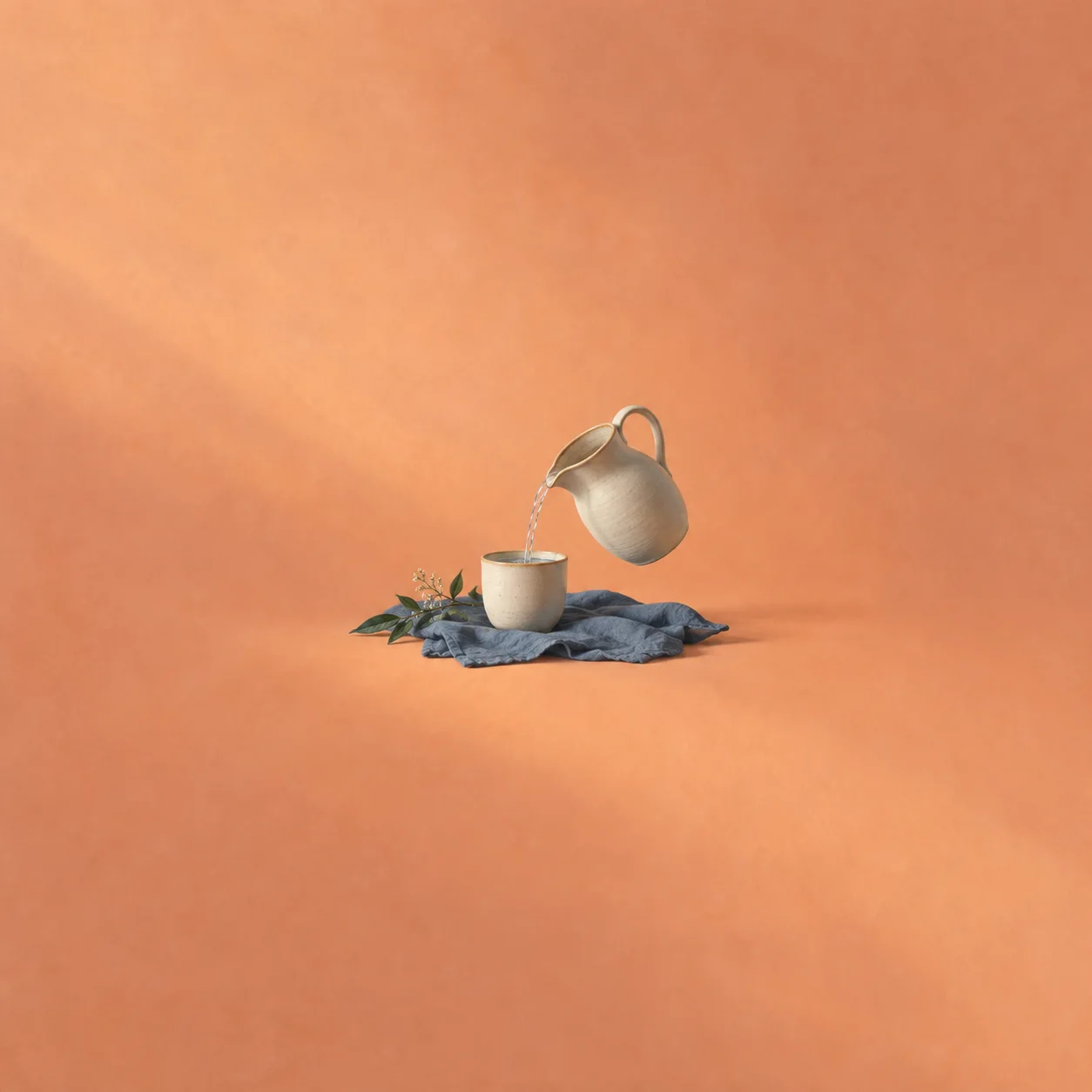 A plain ceramic pitcher pours water into a cup on blue cloth against apricot.