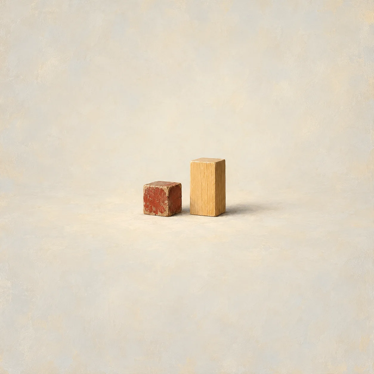 A small scuffed wooden block standing beside a taller, spotless block in warm colours on a plain background.