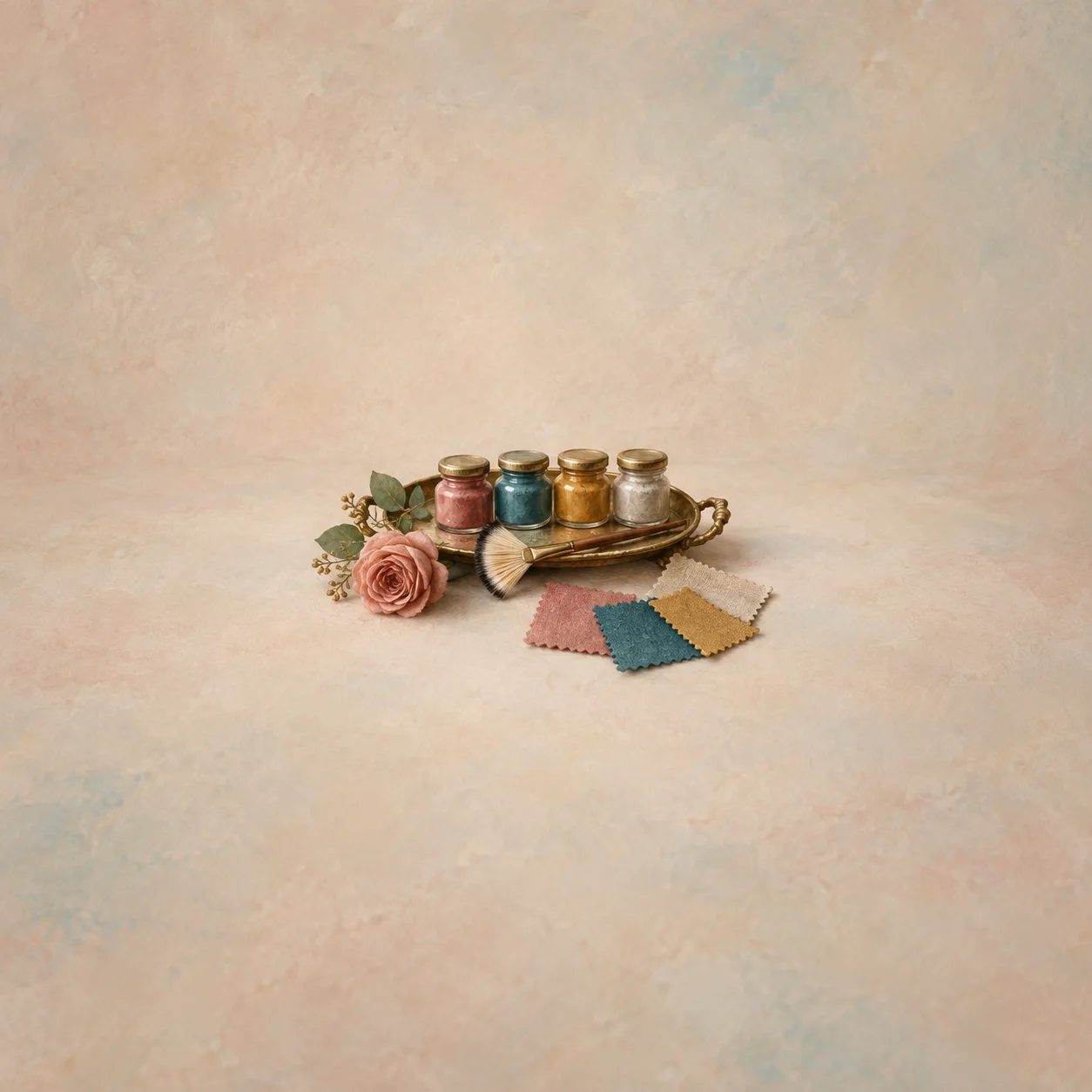 A tray with small pigment pots and a brush beside loose colored fabric squares.