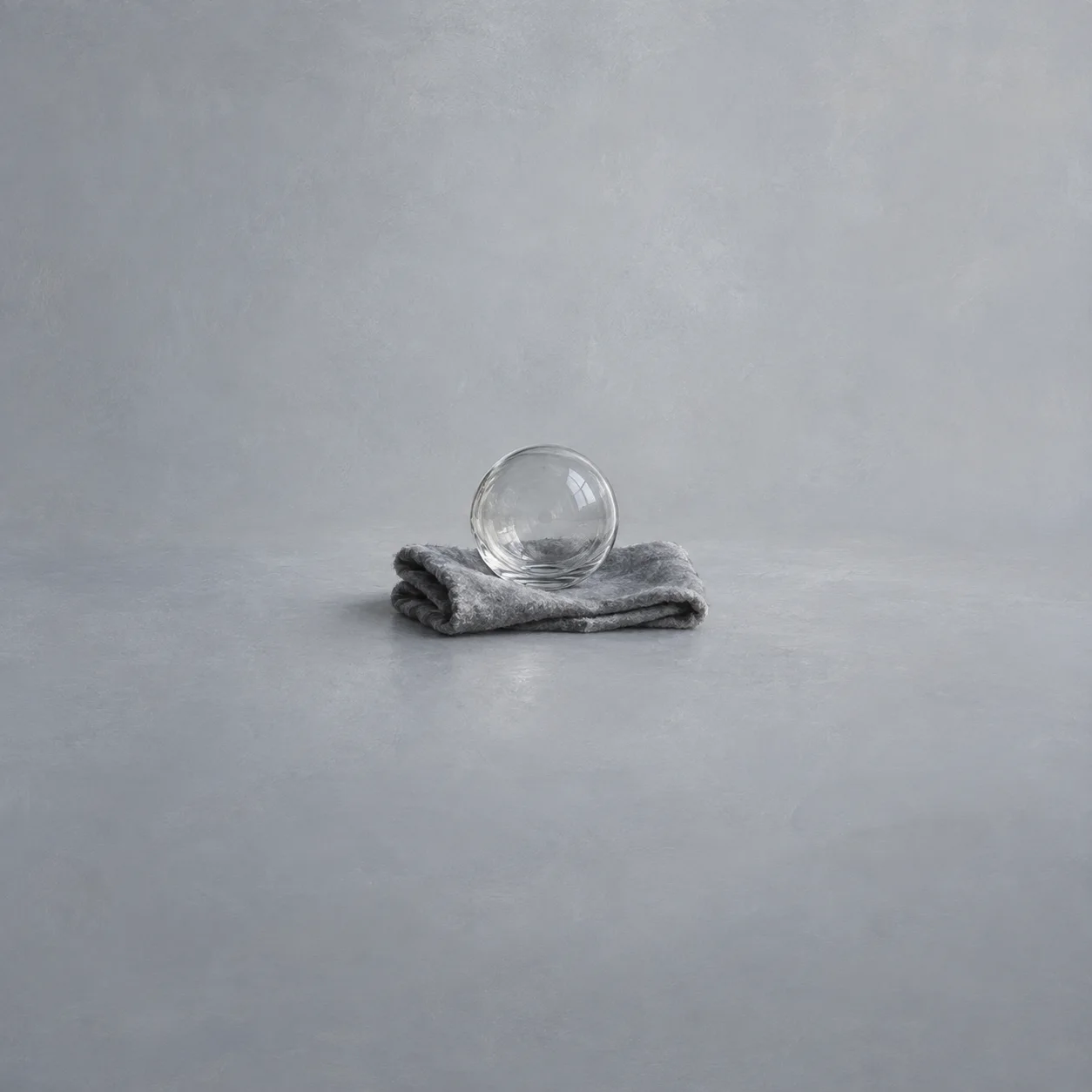 A clear glass sphere sitting on folded grey cloth.