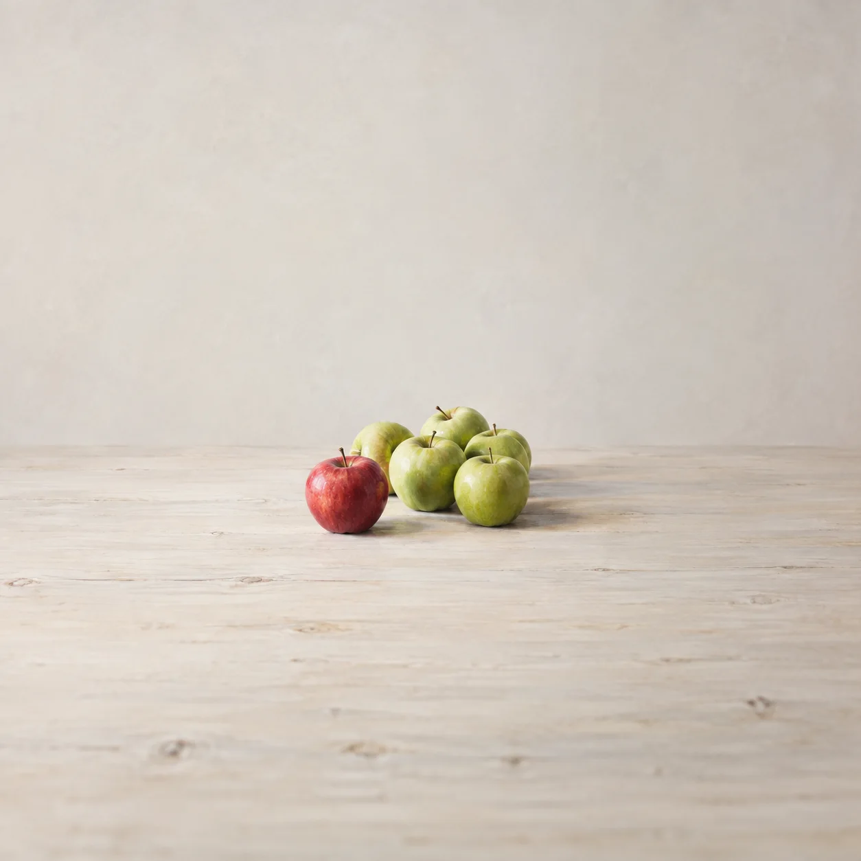 Painterly one red apple beside a small group of green apples on pale wood.